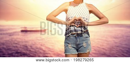 Woman making heart shape with hands  against boat on sea against sky