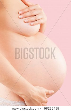 Beautiful pregnant women with big belly. Pink background. Pregnancy and motherhood. 9th month third trimester pregnant belly before birth.