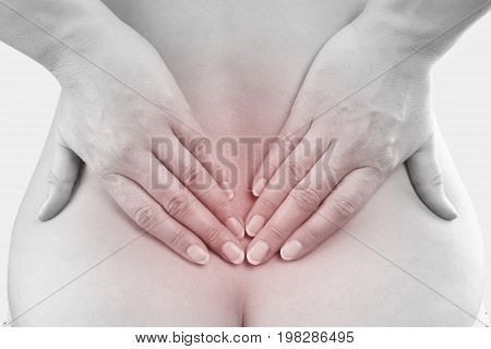 Chronic back pain. Beautiful woman touching lower back with both hands highlighted pain area.