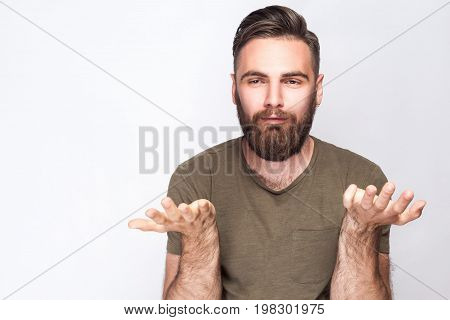 I don't know! Portrait of confused bearded man with dark green t shirt against light gray background. studio shot.