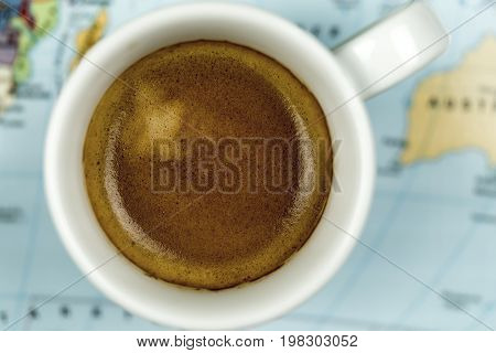 Cup of freshly brewed espresso coffee viewed close up from above on a world map background