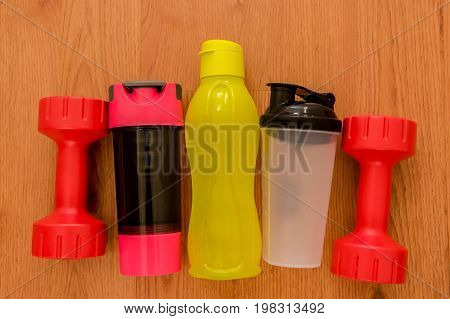 Athlete's set with two pink dumbbells, and a three bottles of water, in a row on wooden background.