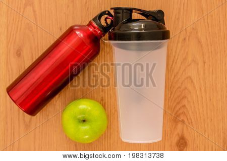 Athlete's green apple, bottle of water and a red thermocafe on wooden background.