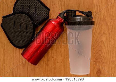 Athlete's set with female clothing, bottle of water and a red thermocafe on wooden background.
