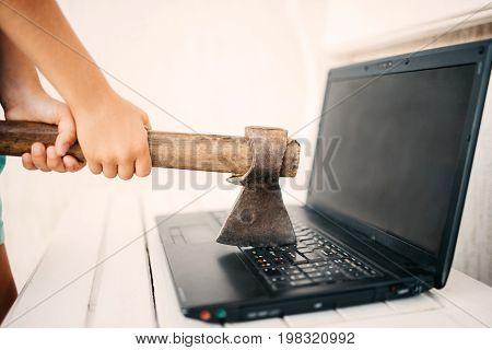 Hands with an ax and a laptop. A boy wants to hit the laptop with an ax