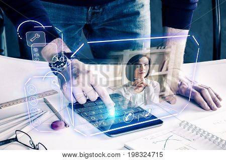 Man with pad leaning on desk at workplace and communicating with young woman via abstract futuristic screen hologram. Concept of network communication family technology augmented reality and future