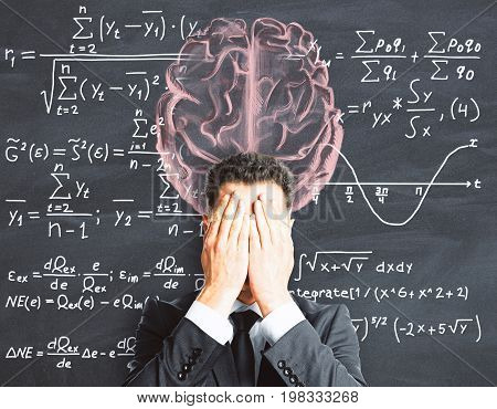 Stressed businessman with drawn brain on chalkboard background with mathematical formulas. Brainstorming and science concept