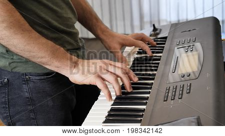 Side view of male musician playing electric piano or electronic keyboard or synthesizer at home.