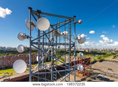 Telecommunication tower with TV antennas satellite dish microwave and panel antennas of mobile operators is located on the roof and city landscape as background
