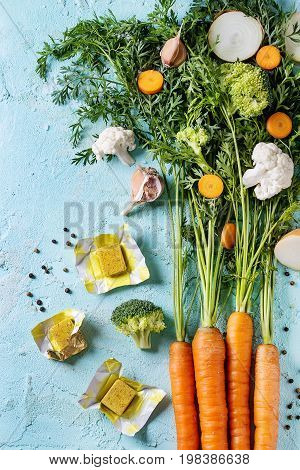 Raw vegetables and bouillon cubes for cooking soup. Young carrot with haulm, broccoli, cauliflower, onion, garlic, salt pepper over turquoise concrete background. Top view. Dinner cooking concept