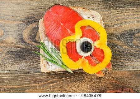 Delicious homemade smoked salmon canapes with cream garnished with a fresh rosemary leaf on dark wooden background. Seafood eating concept.