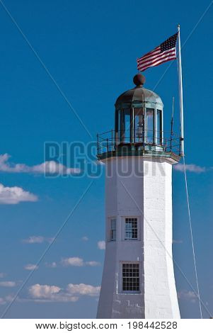 Flag waves over Scituate lighthouse tower in Massachusetts. Scituate Lighthouse is still the oldest complete lighthouse, in the country.