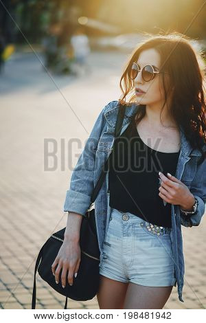 A beautiful young girl with curly hair and glasses wallking in the city