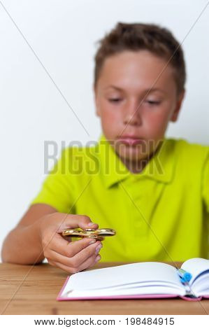 Tween school boy playing fidget spinner while doing homework lessons at home. School education