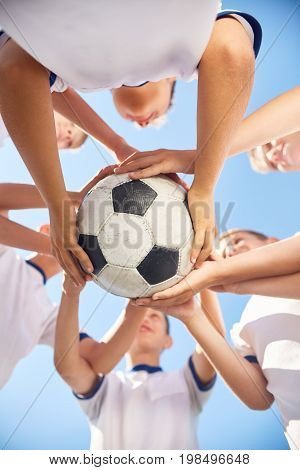 Low angle view of boys in junior football team holding ball together against clear blue sky