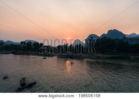 The colorful sunset over Nam Song River with people's silhuoutte swimming in Vang Vieng Laos.