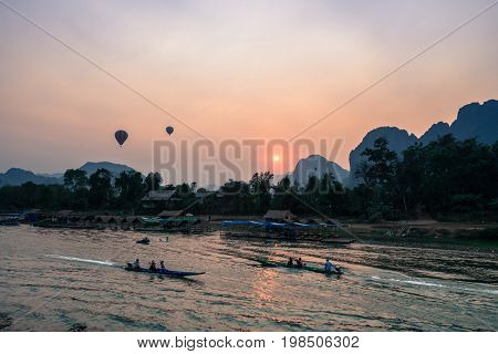 Horizontal picture of sunset over Nam Song River with two hot air ballons and tourists on the boat in Vang Vieng Laos.