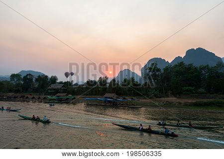 Many boats on Nam Song River with tourists to see the amazing sunset of Vang Vieng over the mountains Laos.