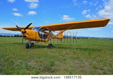Light sport yellow airplane stands on grass against a blue sky