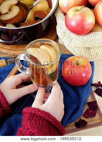 Apple compote. Female hands in a red sweater are holding a glass of warm compote. Saucepan and a sack of apples in the background