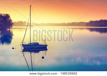 Little sailing boat reflects in the serene water during sunrise. Masuria Poland.