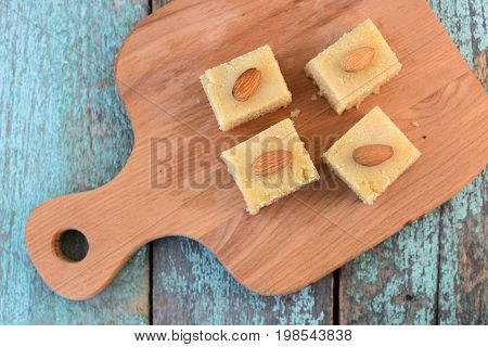 Homemade semolina halva with almonds cut in squares on wooden board top view. Traditional Indian sweets overhead view