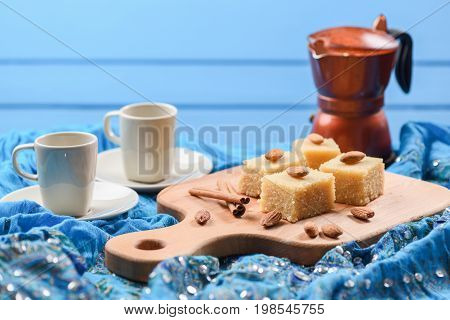 Semolina halva with whole almonds served with geyser coffee maker on blue embroidered cloth. Homemade Indian sweets with blue background