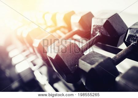 lot of dumbbells stand in row in the gym, glare of light. Concept slimming, musculature, bodybuilding, Sports Equipment.