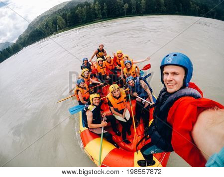 mountain Altai, RUSSIA - July 16, 2017: man in a helmet holds an action camera and makes selfie on the background of friends with oars, rafting