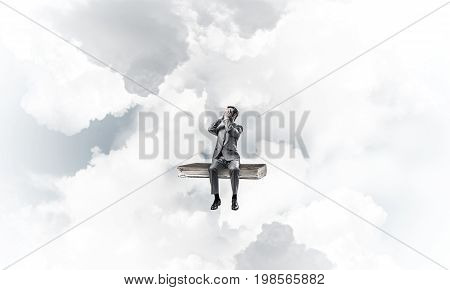 Young shocked businessman sitting on book and covering eyes with palms