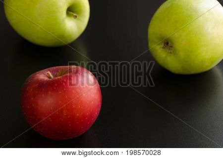 Three apples on a black background. One red apple and two green apples. Selective focus