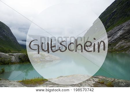 German Text Gutschein Means Voucher. Lake With Mountains In Norway. Cloudy Sky. Peaceful Scenery, Landscape With Rocks And Grass. Greeting Card