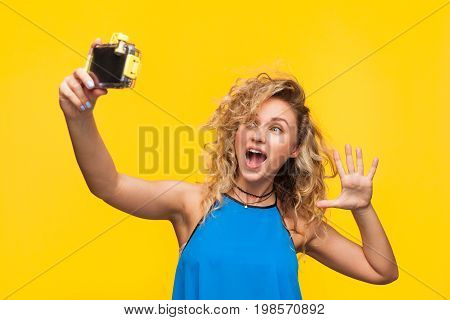 Young curly model on orange background posing expressively taking selfie with camera.