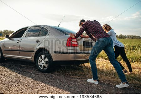 Man and woman pushing a broken car, back view