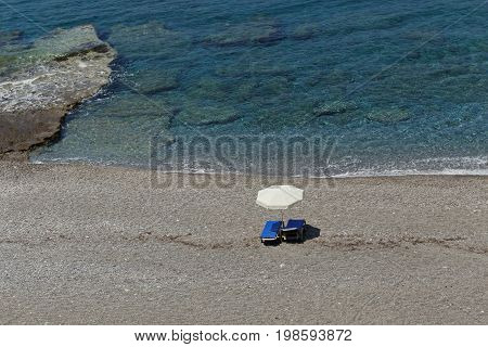 Beautiful sand and pebble beach with crystal clear water and dark blue sunbeds and white umbrella