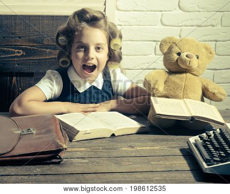 Kid choose career of journalist or writer. Small girl with curler in hair read book. Education and childhood. Child with briefcase and typewriter on table. Little baby secretary in cabinet or library.