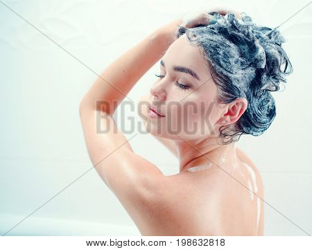 Washing hair. Beautiful naked young woman is smiling and using shampoo while taking shower in bathroom. beauty sexy model girl washing her long black hair