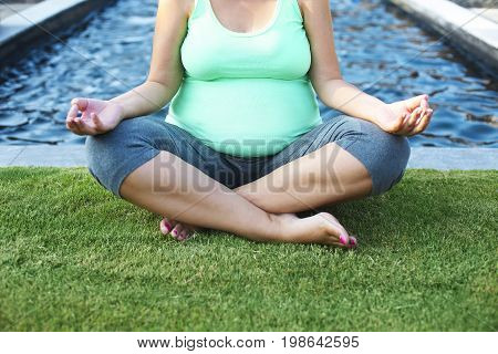 Beautiful pregnant woman meditaiting in summer park. Pregnant yoga