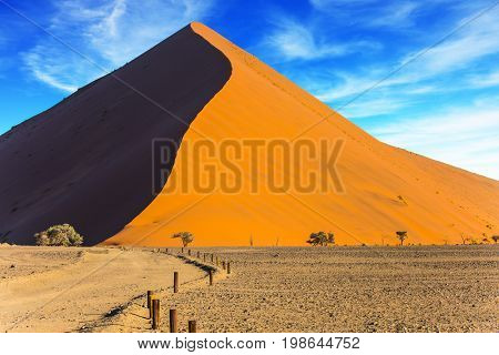 The concept of extreme and exotic tourism. The Namib-Naukluft at sunset. Sharp border of light and shadow over the crest of the dune. Namibia, South Africa