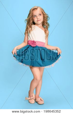 Full length of beautiful little girl in dress standing and posing over blue studio background