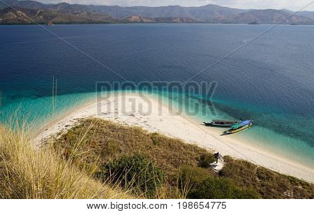 Top View Of Two Boats At The Coast Of A White Sand Beach Surrounded By  Blue Turquoise Colored Ocean