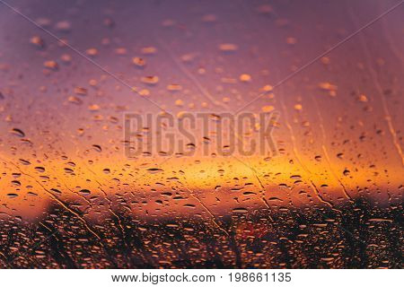 raindrops on car windshield on red sunset with bulred car lights on background