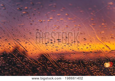 raindrops on car windshield on red sunset with bulred car lights on background