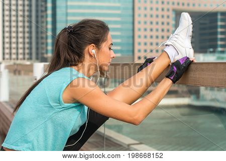 Close up shot of young fitness woman working out on the city street doing exercises, stretching her legs, standing in a vertical split and listening to music in headphones