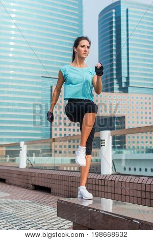 Concentrated young female athlete doing jump step ups exercise on bench on city street