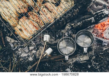 top view on bonfire with chicken meat and cup with water and murshmallows