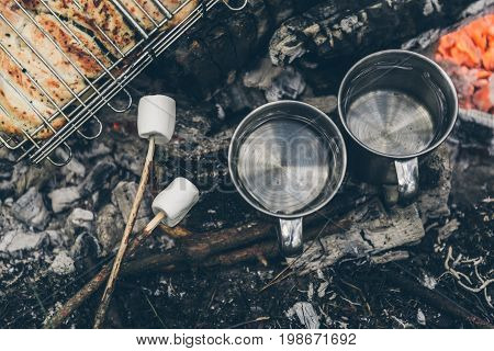top view on bonfire with chicken meat and cup with water and murshmallows