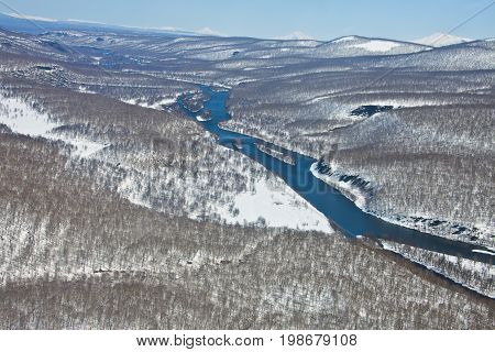 Mountain range after a snowfall and the river in the spring of Kamchatka. The view from the helicopter on the forest and the river in may in far East Russia.