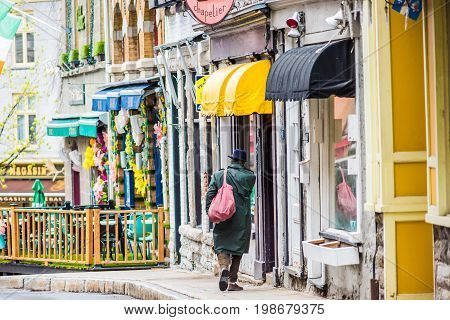 Quebec City Canada - May 30 2017: BiBi & Cie Chapelier store sign with man in coat walking by colorful buildings in old town on Rue Garneau