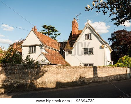 A White Lovely Cottage House In Soft Light And A Brick Wall And Road In Dedham
